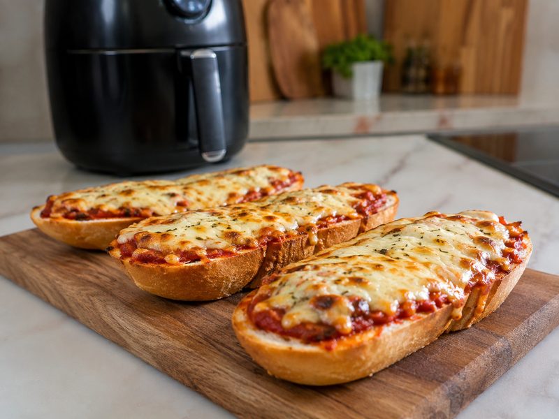 Pizzabroodjes met gesmolten kaas op een houten plank, naast een airfryer